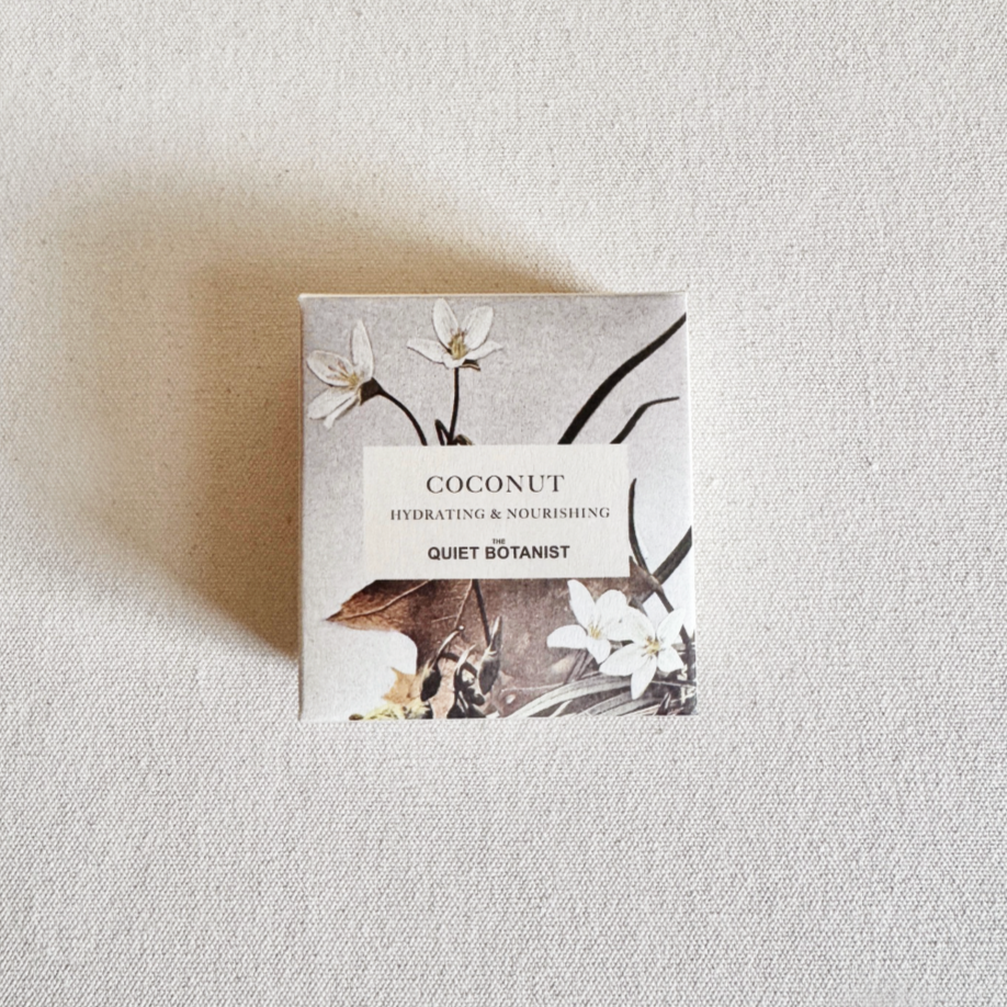 Small box of soap labeled 'Coconut' by 'The Quiet Botanist' on a textured beige background