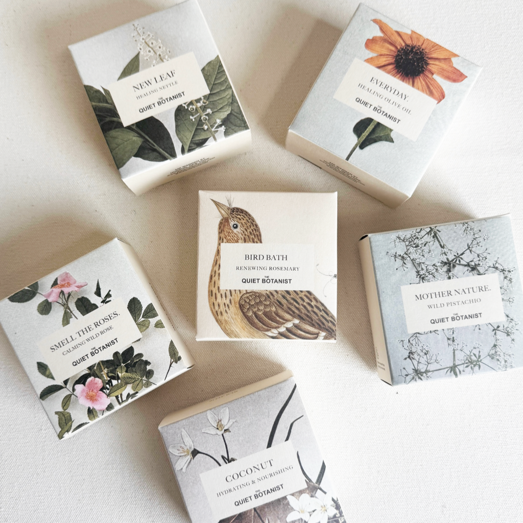 Collection of small soap bars from the Quiet Botanist with decorative packaging featuring nature-themed designs on a light background.